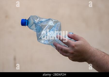 La mano che tiene rotto il flacone di plastica vuoto isolato su uno sfondo sfocato. Concetto di riciclaggio e volontariato. Inquinamento ambientale ed ecolo mondiale Foto Stock