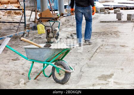 Carriola da costruzione con sabbia e pala per la posa di lastre in cantiere. Foto Stock