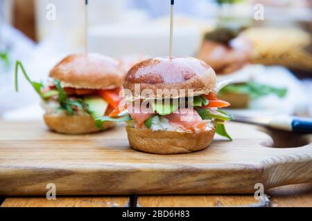 Hamburger con formaggio spalmabile, salmone salato, cale, avocado su panino di grano. Sfondo rustico. Foto Stock