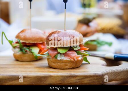 Hamburger con formaggio spalmabile, salmone salato, cale, avocado su panino di grano. Sfondo rustico. Foto Stock