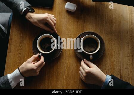 Vista dall'alto due mani da uomo che gesticulano tenendo tazze di caffè su uno sfondo di un tavolo di legno Foto Stock