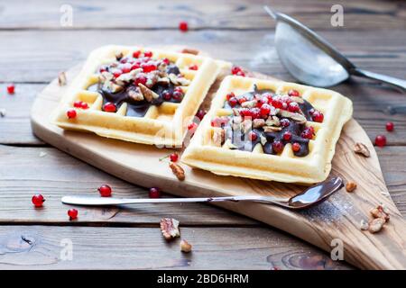 Waffle belgi con salsa al cioccolato, frutti di bosco congelati, noci e polvere di zucchero su un piatto di legno. Rustico sfondo in legno. Foto Stock