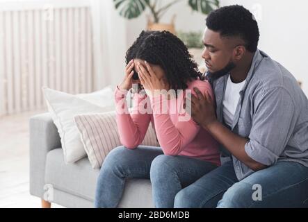 Fidanzato nero attento confortando la sua ragazza sconvolgente piangendo a casa Foto Stock
