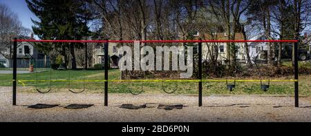 Una fila di altalene per bambini viene roped via con nastro di attenzione giallo brillante che impedisce l'accesso. L'intero parco giochi è stato chiuso a causa della Corona (CO Foto Stock