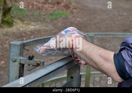 L'uomo usa una borsa di plastica per aprire in modo sicuro un cancello in campagna senza toccare il chiavistello con le mani. Blocco dei coronavirus nel Regno Unito Foto Stock