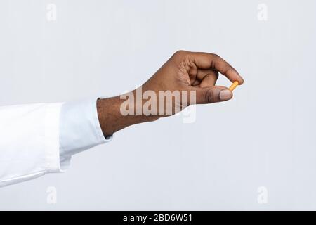 Primo piano della mano nera del medico che tiene una singola pillola Foto Stock