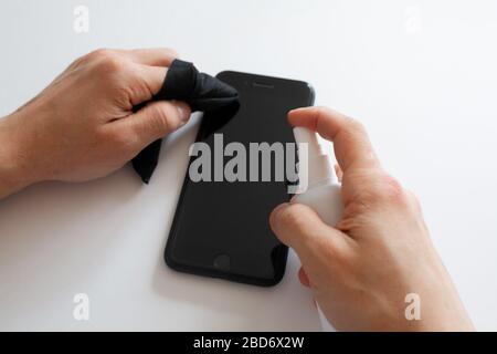 La mano della donna sta spruzzando alcol, disinfettante spray sul telefono cellulare, prevenire l'infezione del virus Covid-19, la contaminazione di germi o batteri, pulire o pulire il telefono per eliminare, scoppio di Coronavirus Foto Stock