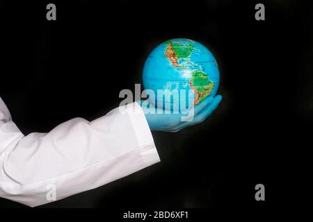 Globo nelle mani di un medico in un gown medico su uno sfondo nero. Il concetto di una pandemia virale covid-19. Epidemia di coronavirus 2020. Foto Stock