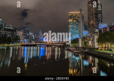 Città moderna di notte con alta linea commerciale su entrambi i lati del fiume Yarra a lunga esposizione e luci che riflettono la superficie liscia dell'acqua. Foto Stock