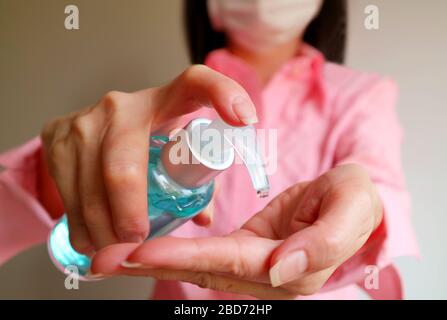 Donna con maschera facciale tenere una bottiglia di gel detergente alcol per lo sfregamento delle mani per prevenire l'infezione Foto Stock