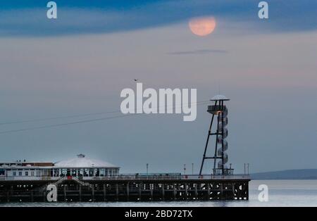 Bournemouth, Regno Unito. 7 aprile 2020. La Super Pink Moon sorge sopra il molo di Bournemouth a Dorset. Credit: Richard Crease/Alamy Live News Foto Stock