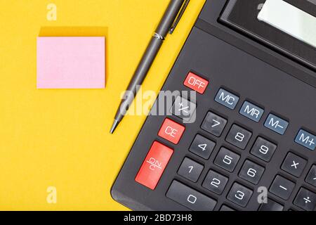 Calcolatrice, penna e nota adesiva vuota su sfondo giallo. Contesto economico o aziendale. Spazio di copia. Mock up Foto Stock