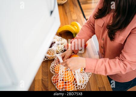 Donna che tiene l'acquisto di frutta nella sua cucina. Utilizzando un sacchetto riutilizzabile in rete di cotone organico su sfondo di legno. Zero sprechi, concetto senza plastica. S Foto Stock