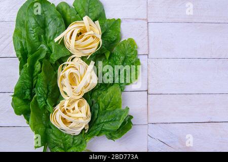 Tagliatelle di spinaci e pasta su sfondo di legno bianco, studio fotografico. Viste dall'alto con spazio libero Foto Stock