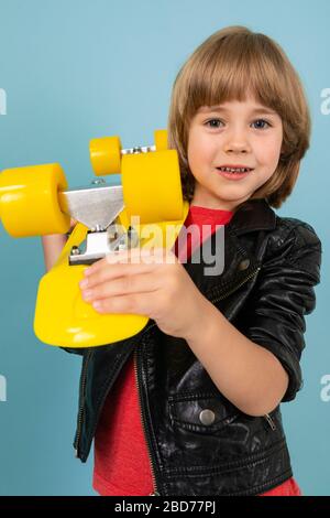 ragazzo tiene in mano uno skateboard giallo su sfondo blu Foto Stock