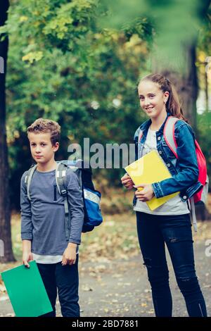 Ritorno a scuola. Chiudi due amici felici con zaini che ridono e si divertono nel parco. Ragazzo e ragazza che tiene libri il primo giorno di scuola. Foto Stock