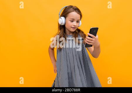 la bambina ascolta la sua musica preferita con le cuffie su uno sfondo arancione Foto Stock