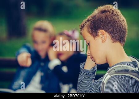 Triste ragazzo sentendosi lasciato fuori, stuzzicato e bullizzato dai suoi compagni di classe. Ragazzo infelice che ha problemi di adattamento con gli altri a scuola. Foto Stock