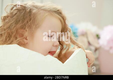 Un piccolo bambino piccolo è seduto in un uovo bianco che si schiuse contro uno sfondo colorato studio per un ritratto neonato o concetto di famiglia. Foto Stock