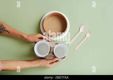 Mani che mettono le tazze di canna da zucchero con i supporti di carta con gli utensili di bambù Foto Stock