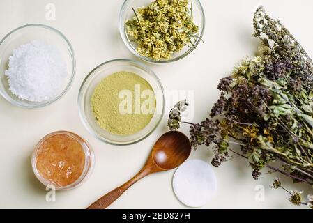 Un bouquet di fiori secchi, un cucchiaio di legno e ciotole di vetro con prodotti naturali per mescolare e creare maschere e creme naturali. Foto Stock