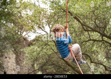 Il bambino di quattro anni sorride appeso a una corda con le mani Foto Stock