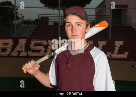 Ritratto di un giocatore di baseball della High School in uniforme di maroon che tiene il suo mat Foto Stock