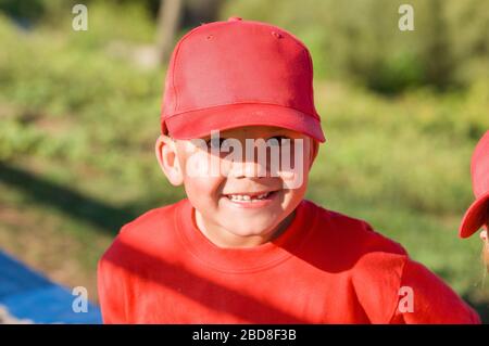 Il ragazzo manca un dente nel cappello rosso di baseball sorridente alla macchina fotografica Foto Stock