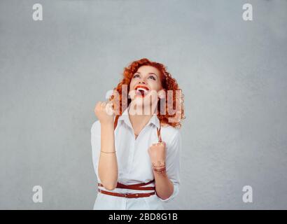 Vincitore. Happy redhead ricci donna exults pompando pugni estatico celebra il successo mani gesto isolato su sfondo grigio. Emozione umana positiva, Foto Stock