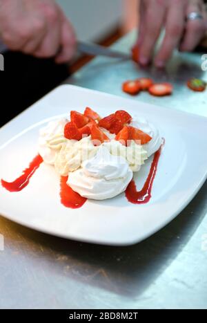 chef che prepara paillova con fragole fresche e panna Foto Stock