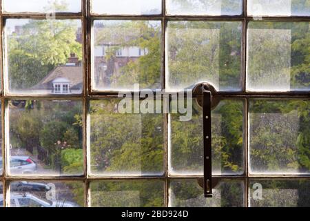 Case inglesi e alberi visti attraverso una polverosa finestra in metallo lavorato in ferro battuto Foto Stock