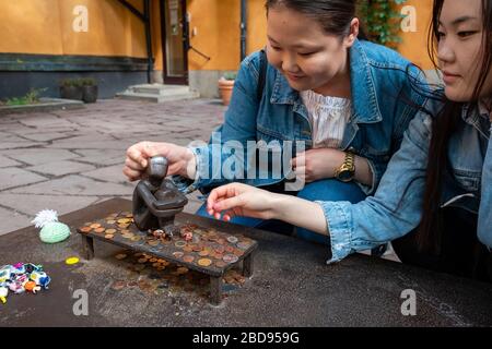 Due turisti asiatici che toccano la piccola scultura di Järnpojke o di Iron Boy per fortuna, Stoccolma, Svezia, Europa Foto Stock