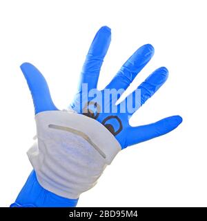 Mano con guanto chirurgico Blue con una maschera facciale raffigurante un viso con riferimento alla protezione medica contro il virus corona , covid 19. Foto Stock