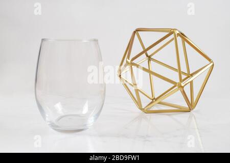 Un lussuoso vetro di vino senza gambo si brividi su uno sfondo di marmo bianco accanto ad una moderna scultura d'oro. Ampio spazio per la copia per aggiungere il proprio design a Th Foto Stock