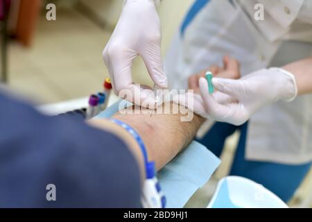 Il processo di prelievo di sangue venoso attraverso un ago per l'analisi in un paziente di un infermiere medico di sesso maschile. Foto Stock