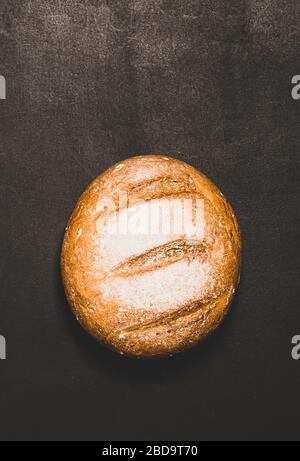 Pane appena sfornato con crosta dorata su sfondo scuro. Concetto di cibo minimalismo. Spazio di copia cornice verticale Foto Stock