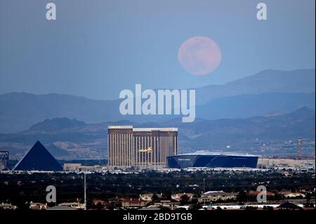 Las Vegas, Nevada, Stati Uniti. 7 Aprile 2020. La luna rosa super, la più grande superluna dell'anno, sorge su (L-R) Luxor Hotel and Casino, Delano Las Vegas al Mandalay Bay Resort and Casino, Mandalay Bay Resort and Casino e lo Stadio Allegiant in costruzione il 7 aprile 2020 a Las Vegas, Nevada. La luna rosa ha ottenuto il relativo nome perché la luna piena di aprile si presenta allo stesso tempo del fiore selvatico rosa Phlox subulata fiorisce in America del Nord. Una superluna si verifica quando una luna piena coincide con il suo perigeo, che è il suo approccio più vicino alla Terra. Credit: David Becker/ZUMA Wire/Alamy Live News Foto Stock