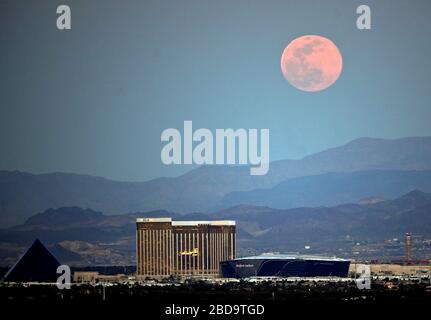 Las Vegas, Nevada, Stati Uniti. 7 Aprile 2020. La luna rosa super, la più grande superluna dell'anno, sorge su (L-R) Luxor Hotel and Casino, Delano Las Vegas al Mandalay Bay Resort and Casino, Mandalay Bay Resort and Casino e lo Stadio Allegiant in costruzione il 7 aprile 2020 a Las Vegas, Nevada. La luna rosa ha ottenuto il relativo nome perché la luna piena di aprile si presenta allo stesso tempo del fiore selvatico rosa Phlox subulata fiorisce in America del Nord. Una superluna si verifica quando una luna piena coincide con il suo perigeo, che è il suo approccio più vicino alla Terra. Credit: David Becker/ZUMA Wire/Alamy Live News Foto Stock