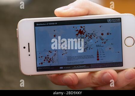 La mano tiene il telefono, sullo schermo del quale le informazioni sulla diffusione del coronavirus nel mondo. Utilizzo delle tecnologie mobili. Foto Stock