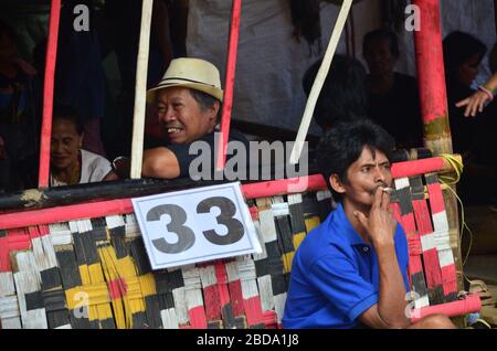 Visitatori e parenti partecipano a una cerimonia funeraria a Tana Toraja, Indonesia. Un uomo sta fumando. Foto Stock
