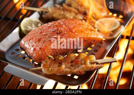 Frutti di mare conditi e pronti per grigliare su un barbecue con una spessa e succosa bistecca di salmone e kebab di gamberi visti da vicino Foto Stock