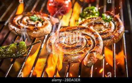 Spirali di salsiccia piccante alla griglia su un barbecue su bollente costolette con peperoncino e pomodori in primo piano Foto Stock