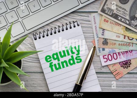 FONDI AZIONARI testo con blocco note, tastiera, vaso decorativo, penna stilografica e banconote valuta su sfondo di legno. Concetto di business e copy space Foto Stock
