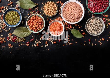 Assortimento di legumi, girato dall'alto su uno sfondo nero con spazio di copia. Lenticchie, soia, ceci, fagioli rossi, una ventata di impulsi Foto Stock