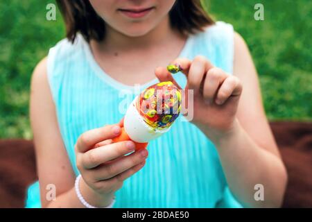 Ragazza piccola cute sta dipingendo l'uovo di Pasqua con il suo dito, foto ravvicinata tagliata con fuoco designato sull'uovo Foto Stock