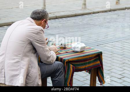 Il vecchio è seduto e sta giocando al telefono. Per strada. Invia il cobble. Foto Stock