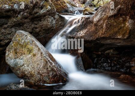 Limpido torrente di montagna che scorre tra grandi massi in una foresta sulle montagne della Corsica Foto Stock