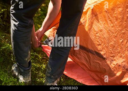 Guida passo passo su come allestire una tenda. I turisti posano una tenda in un campeggio. Uomo che raccoglie una tenda arancione nella foresta Foto Stock