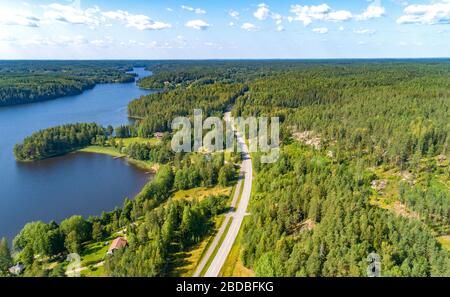 Veduta aerea della strada tra la foresta verde estiva e il lago blu in Finlandia Foto Stock