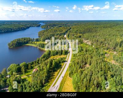 Veduta aerea della strada tra la foresta verde estiva e il lago blu in Finlandia Foto Stock